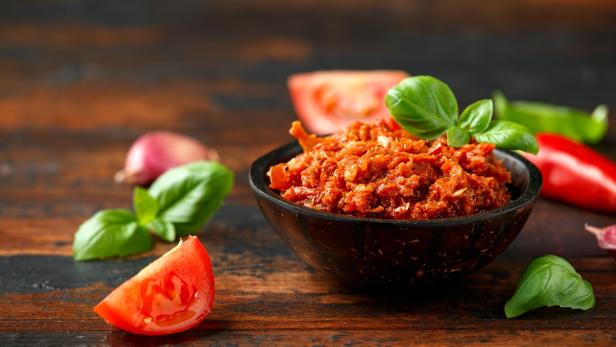 Ein Schälchen Pesto Rosso mit Basilikum, Tomaten und Chili auf einem Holztisch.