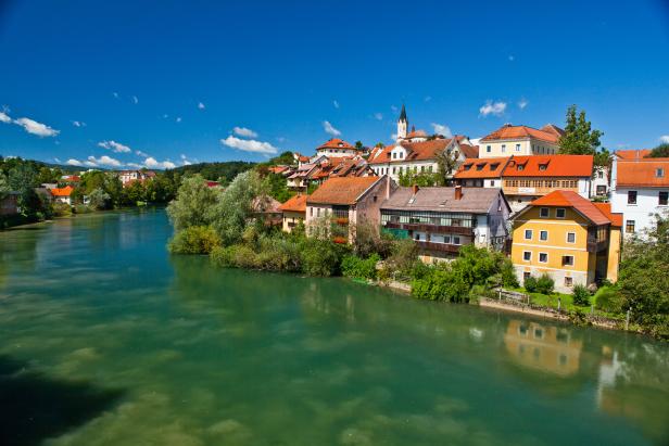 Die Stadt Škofja Loka in Slowenien liegt an einem Fluss unter blauem Himmel.