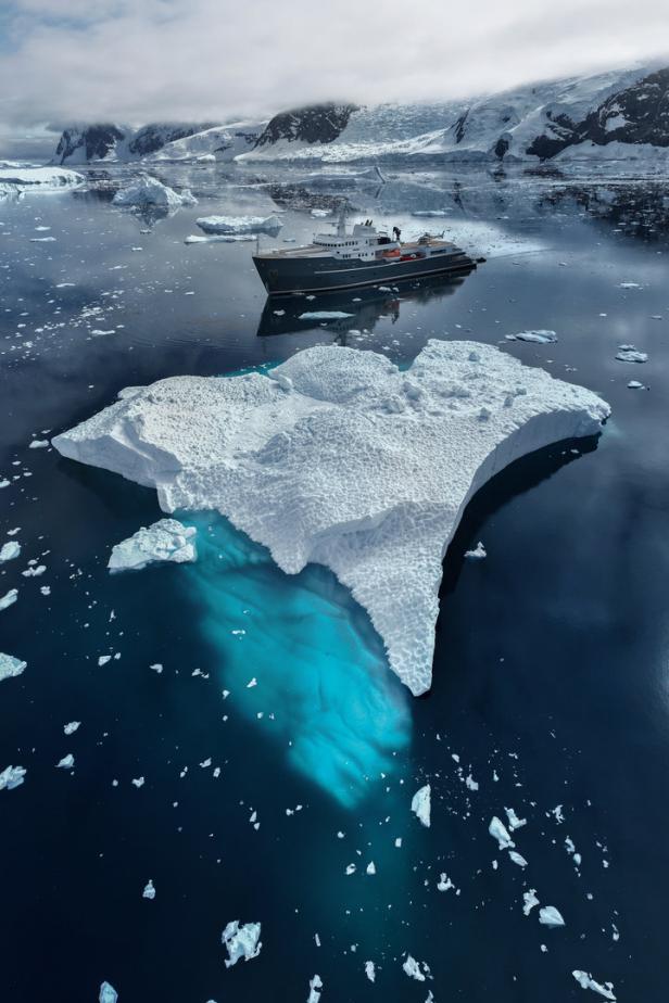 Ein Schiff fährt an einem großen Eisberg in einer eisigen Landschaft vorbei.