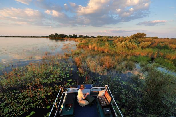 Eine Person fährt mit einem Boot durch ein von Vegetation gesäumtes Gewässer.