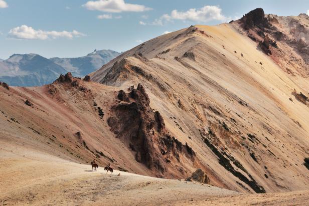 Zwei Reiter hoch oben in einer sandfarbenen Berglandschaft.