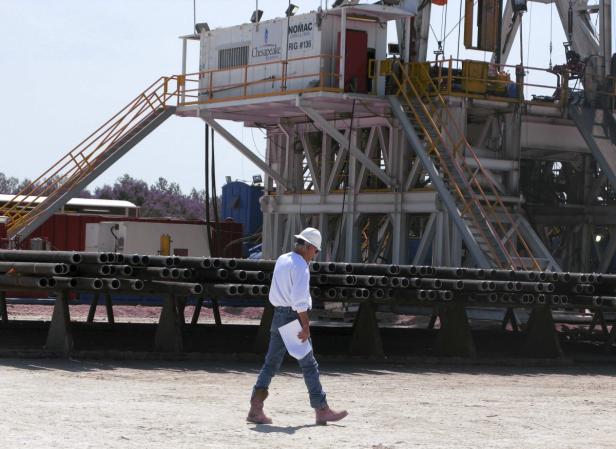Ein Arbeiter mit Helm geht an einem Ölbohrturm vorbei.
