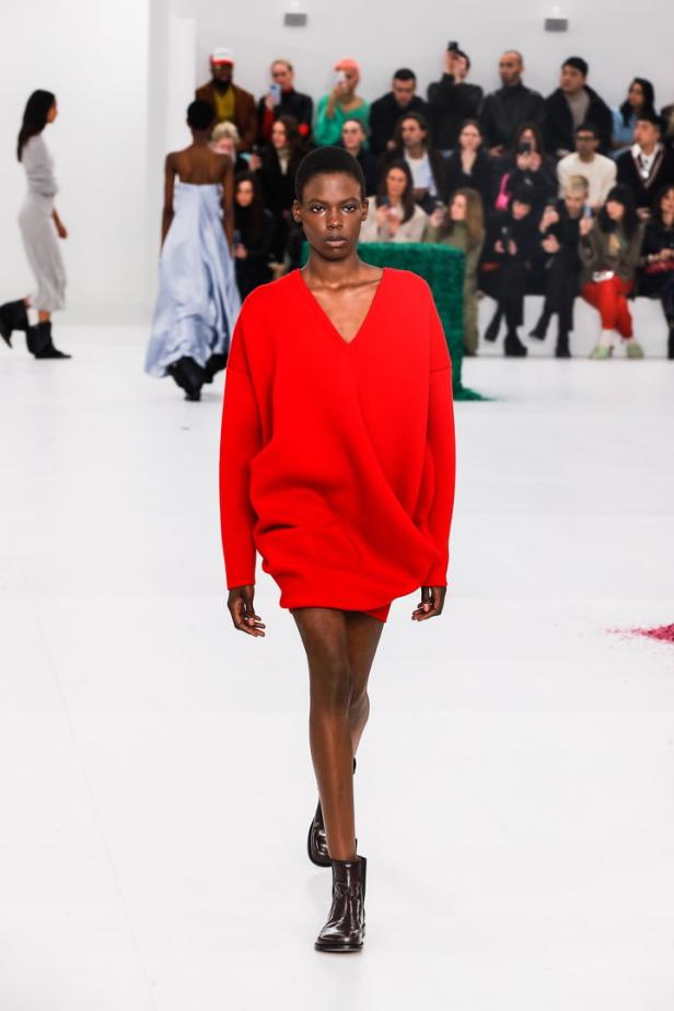 Eine Frau präsentiert ein rotes Kleid und Stiefeletten auf dem Laufsteg der Loewe Herbst/Winter 2023/24 Kollektion.
