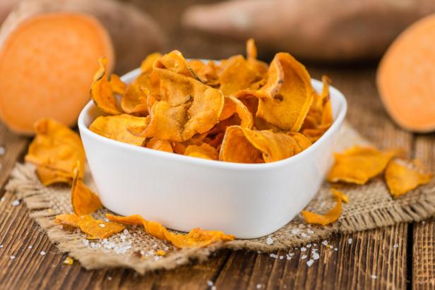 Süßkartoffelchips in einer weißen Schale auf einem Holztisch.