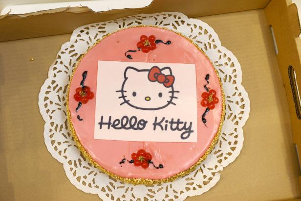 Ein runder, rosa Kuchen mit einem „Hello Kitty“-Motiv in einer Pappschachtel.
