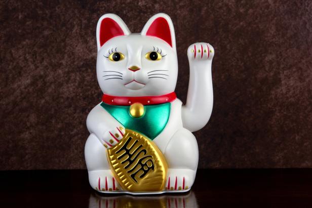 Eine winkende Maneki Neko, eine japanische Glückskatze, hält eine goldene Tafel.