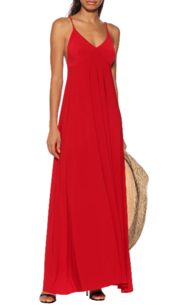 Eine Frau trägt ein rotes, bodenlanges Kleid und hält einen Strohhut.