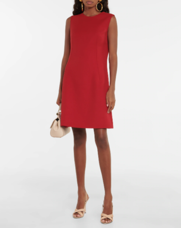 Eine Frau in einem roten, ärmellosen Kleid, mit einer Handtasche und Sandalen.