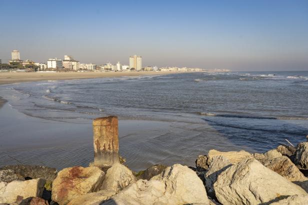 Blick auf einen Strand mit Gebäuden im Hintergrund und Felsen im Vordergrund.