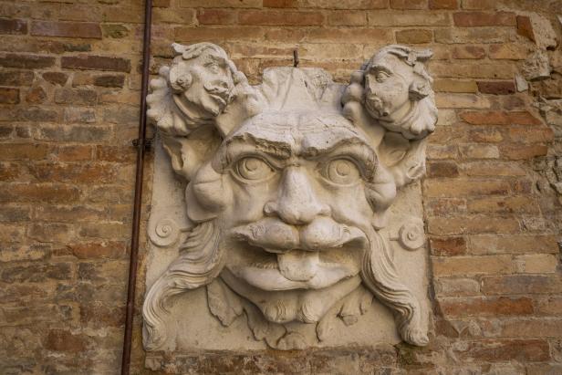 Eine steinerne Maske mit fratzenhaftem Gesichtsausdruck an einer Ziegelmauer.