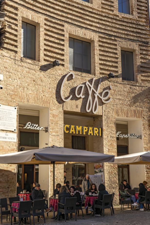 Ein Straßencafé mit Gästen vor einem Gebäude mit der Aufschrift „Caffè Campari“.