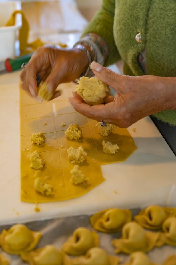 Eine Person füllt gelbe Tortellini mit einer hellen Füllung.