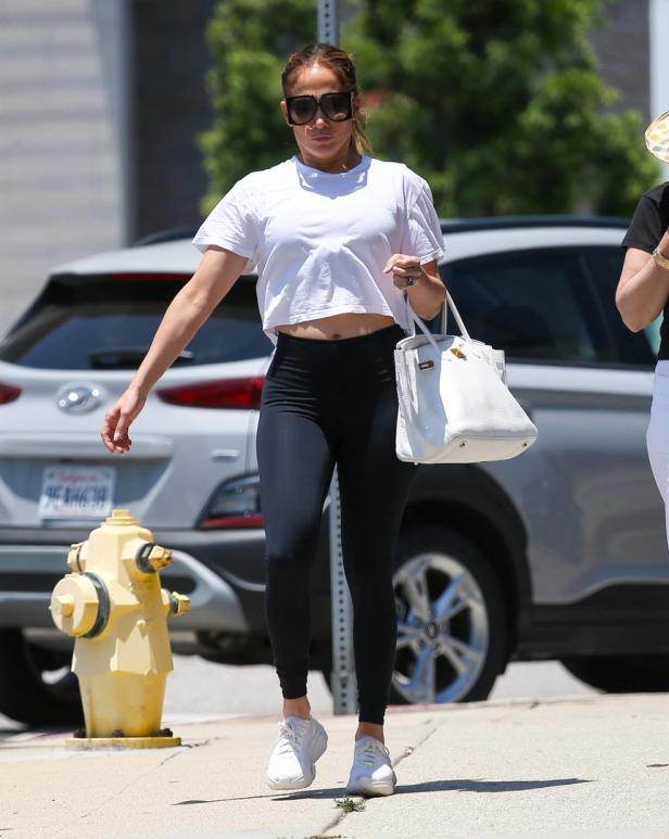 Jennifer Lopez geht mit einer weißen Handtasche und Sportkleidung die Straße entlang.