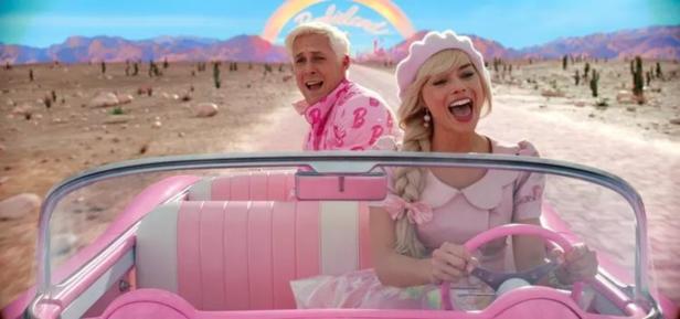 Margot Robbie und Ryan Gosling fahren in einem pinkfarbenen Auto durch eine Wüstenlandschaft.
