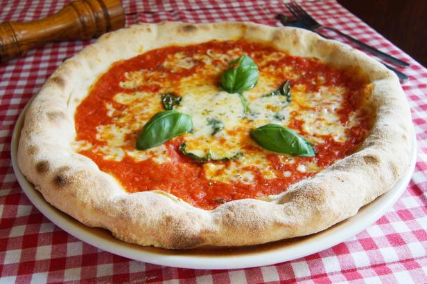 Eine Pizza Margherita mit Basilikum auf einem rot-weiß karierten Tisch.
