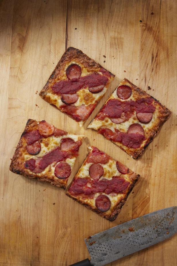 Vier Stücke Detroit-Pizza mit Wurst auf einem Holzbrett.