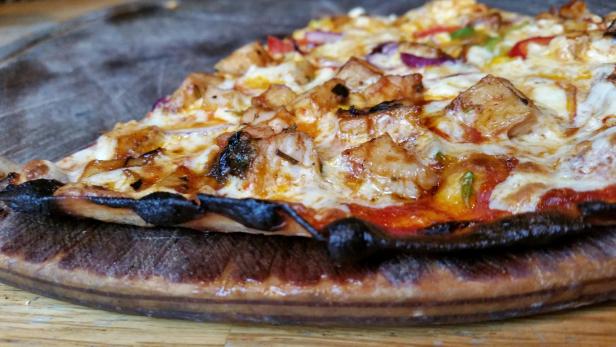 Nahaufnahme einer Pizza mit Hähnchen, Paprika und roten Zwiebeln.