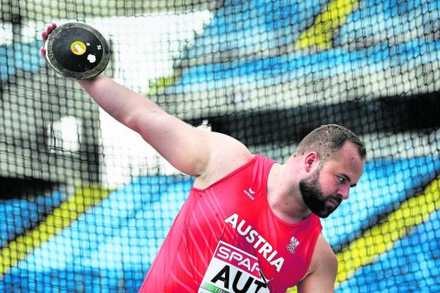 Ein Diskuswerfer im roten Trikot der österreichischen Nationalmannschaft beim Wettkampf.