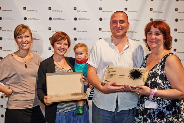 Eine Gruppe von Personen hält eine Auszeichnung der ERSTE Stiftung in den Händen.