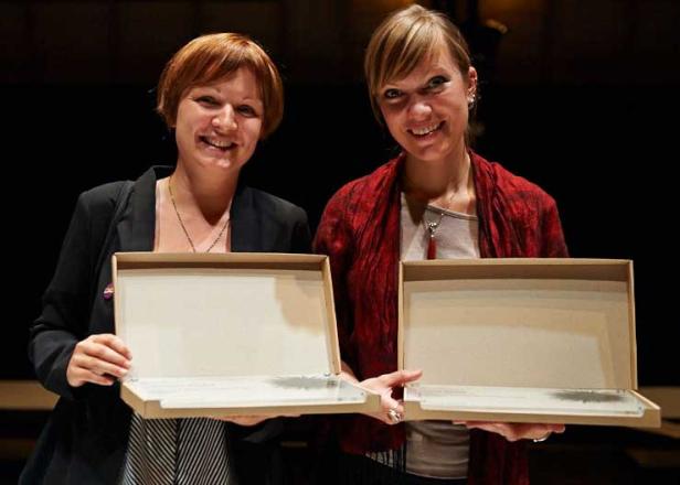 Zwei Frauen halten lächelnd Auszeichnungen in ihren Händen.