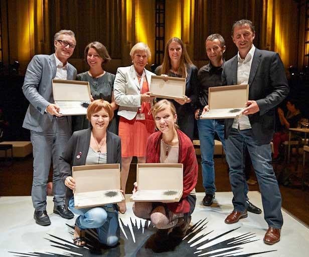 Eine Gruppe von Menschen posiert mit offenen Kisten auf einer Bühne.