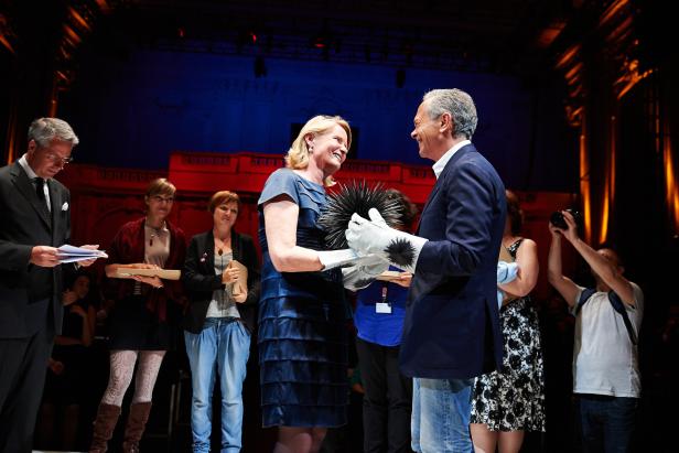 Eine Frau in einem blauen Kleid erhält eine Auszeichnung in Form eines Seeigels.