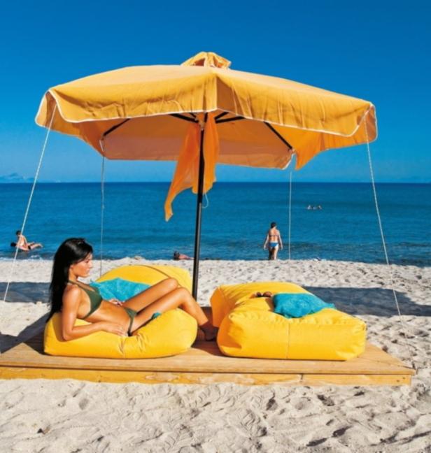 Eine Frau entspannt am Strand unter einem gelben Sonnenschirm auf einem gelben Sitzsack.
