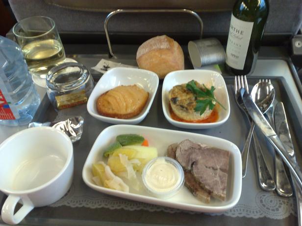 Ein Flugzeugtablett mit einer Mahlzeit, inklusive Brötchen, Wein und verschiedenen Beilagen.