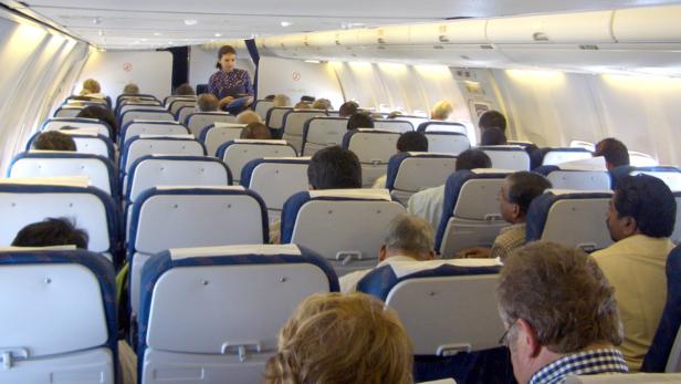 Eine Flugbegleiterin steht im Gang eines vollbesetzten Flugzeugs.