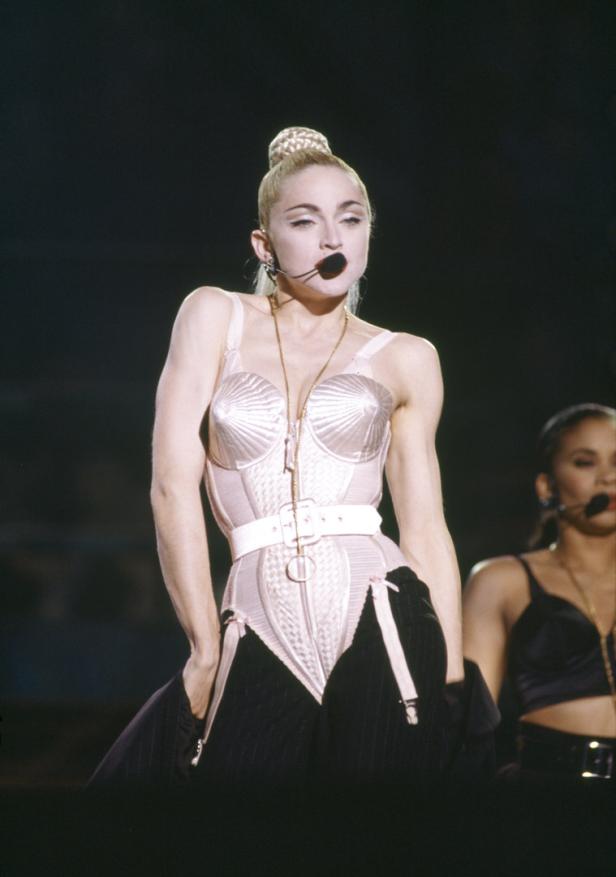 Madonna tritt in einem rosa Korsett und schwarzen Hosen auf einer Bühne auf.