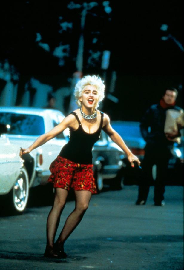 Madonna tanzt in einem schwarzen Top und einem roten Rock auf der Straße.