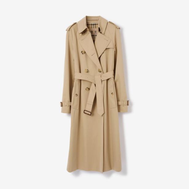 Ein beigefarbener Trenchcoat mit Gürtel hängt vor einem weißen Hintergrund.