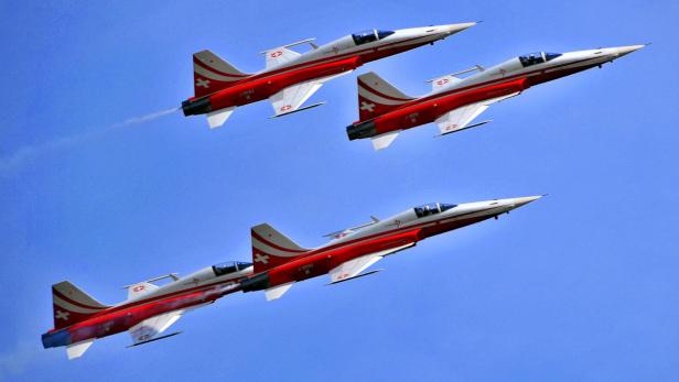 Vier rote und weiße Kampfflugzeuge fliegen in Formation am Himmel.