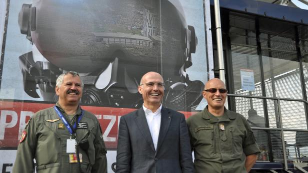 Drei Männer posieren vor einem Poster mit einem Flugzeugcockpit.