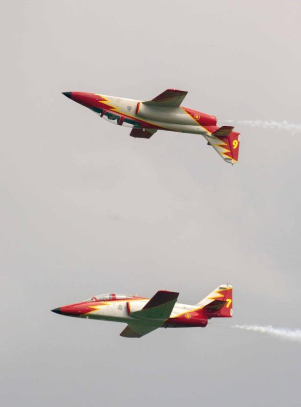 Zwei rot-weiß-gelbe Flugzeuge fliegen im Formationsflug am Himmel.