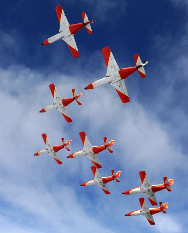 Acht rot-weiße Flugzeuge fliegen in Formation am Himmel.