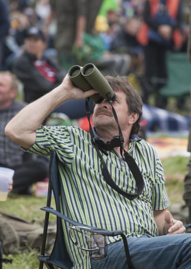 Ein Mann sitzt auf einem Stuhl und schaut durch ein Fernglas.