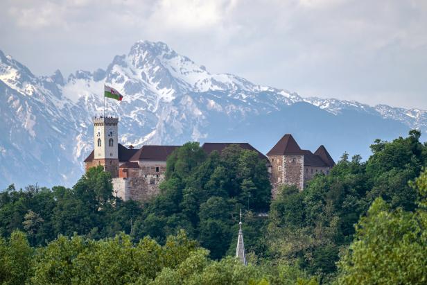 Die Burg von Bled thront auf einem Hügel, im Hintergrund schneebedeckte Berge.
