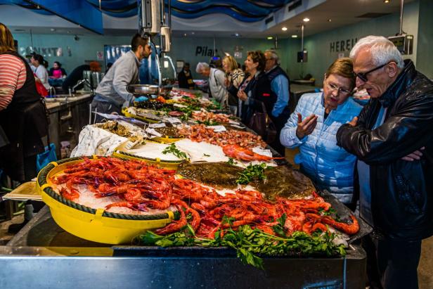 Auf einem Fischmarkt betrachten Kunden eine Auslage mit Meeresfrüchten und Fischen.