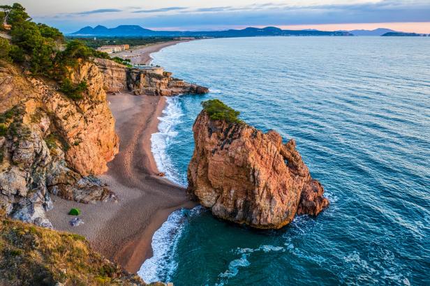 Blick auf eine Küstenlandschaft mit Felsen, Strand und blauem Meer.