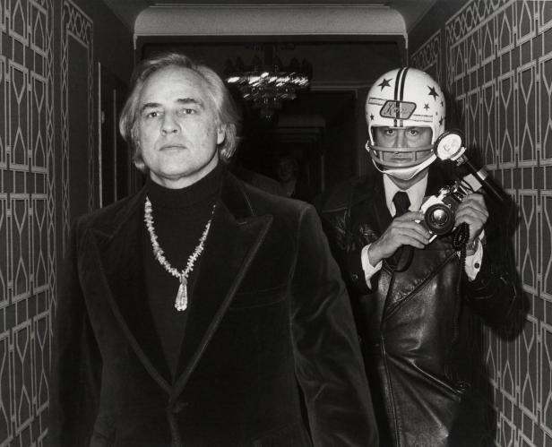Marlon Brando und ein Fotograf mit Footballhelm stehen in einem Flur.