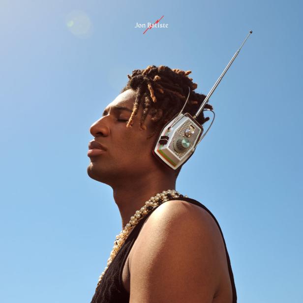 Jon Batiste mit Kopfhörern, die wie ein Radio aussehen, vor blauem Himmel.