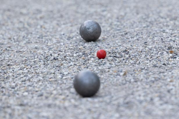 Zwei Boule-Kugeln und eine rote Zielkugel auf einem Kiesplatz.