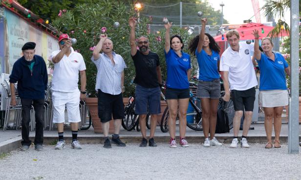 Eine Gruppe von acht Personen spielt Boule im Freien.