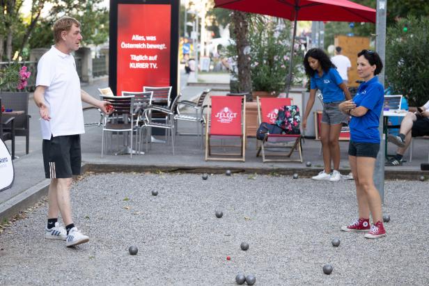 Menschen spielen Boule auf einem Kiesplatz im Freien.