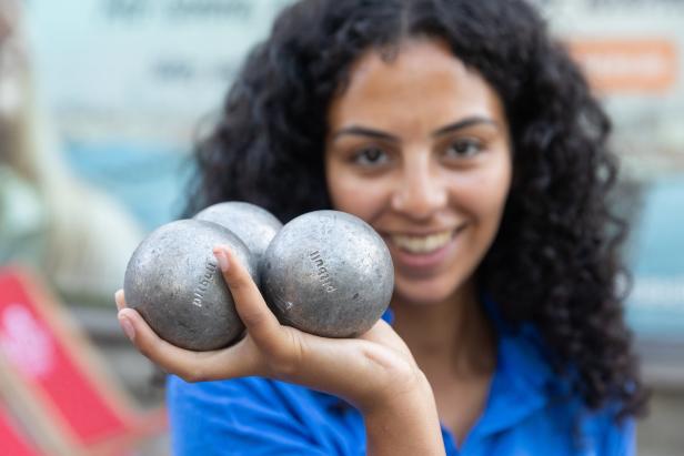 Eine lächelnde Frau hält drei Boule-Kugeln in ihrer Hand.
