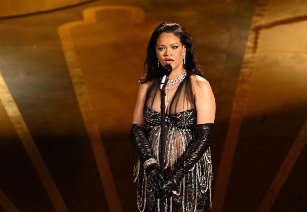 Rihanna singt in einem schwarzen Kleid und langen Handschuhen auf einer Bühne.