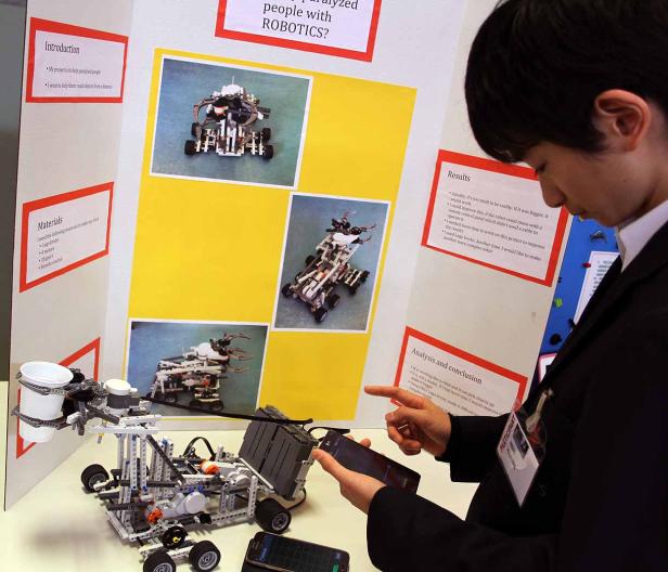Ein Jugendlicher präsentiert einen Roboter aus Legosteinen für ein Schulprojekt.