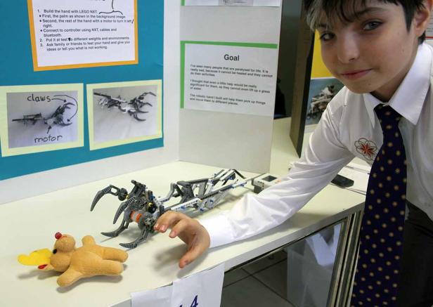 Ein Junge präsentiert eine Roboterhand aus Lego, die einen Plüschtier-Elch greift.