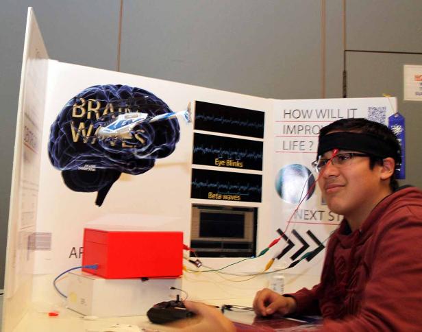 Ein junger Mann mit Stirnband präsentiert ein Projekt über Gehirnwellen.